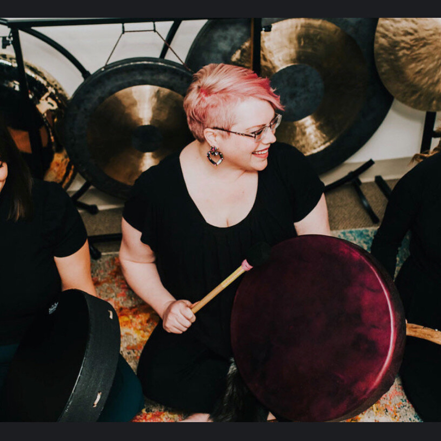Jhill seated with a drum, gongs behind her.